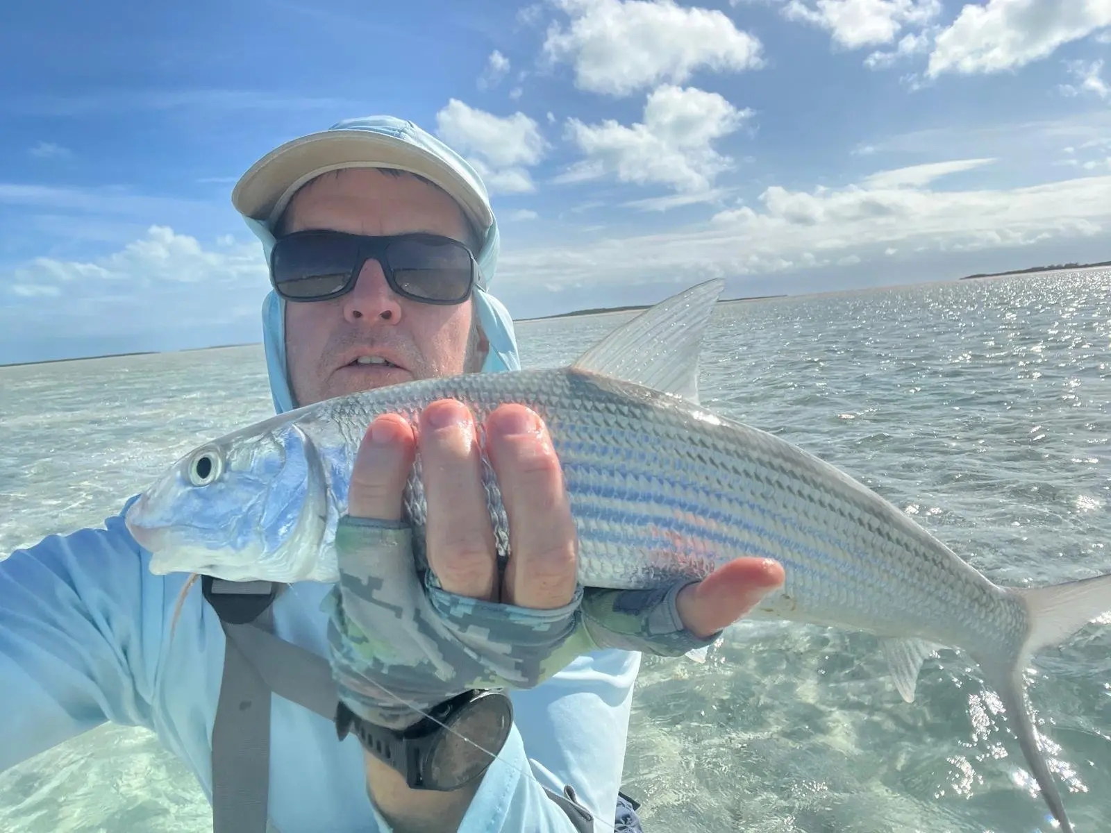 Close-up of a bonefish held carefully over shallow water